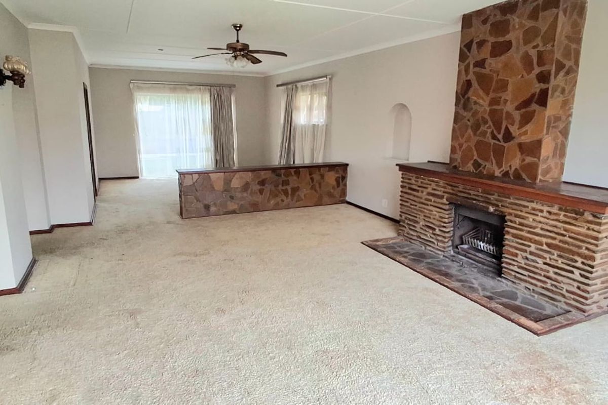 Spacious living room featuring a prominent stone fireplace, stone room divider, and ceiling fan, offering a dated but functional layout ready for modernization.