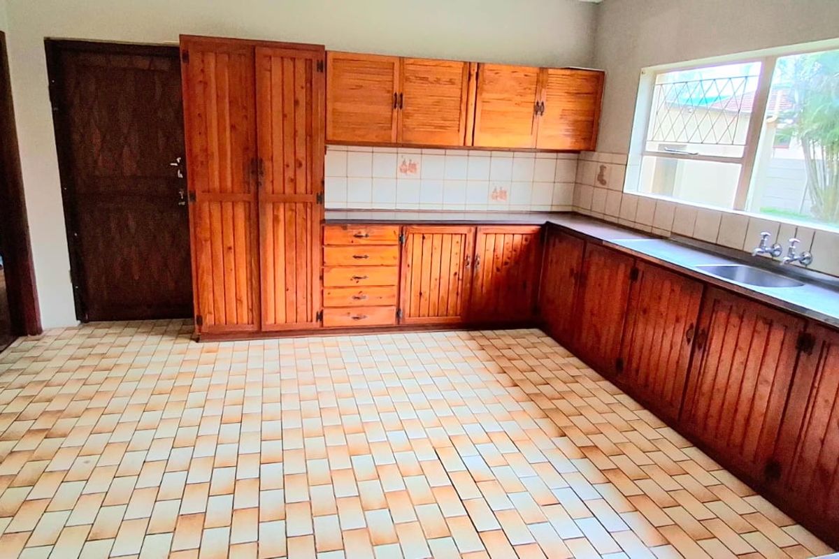 A spacious kitchen featuring traditional wooden cabinetry, tiled flooring, and a large window, offering a functional layout ready for modern updates.