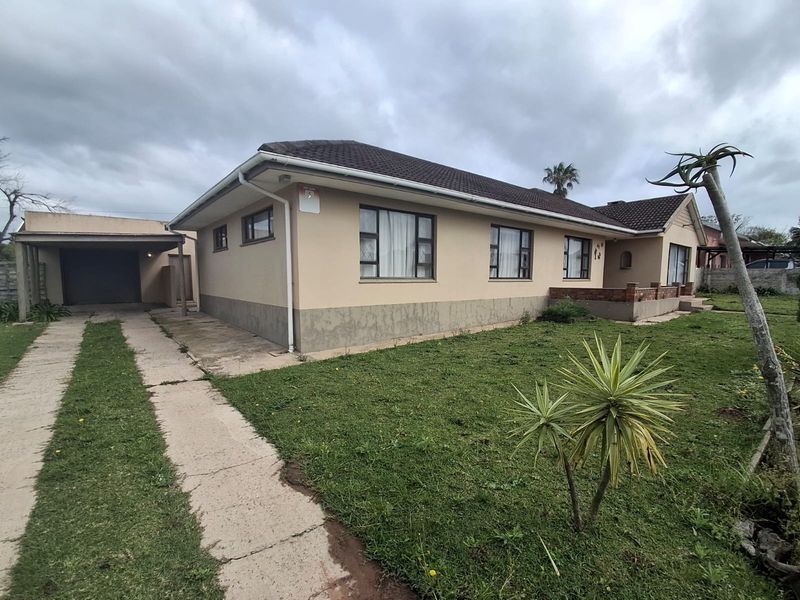 Front view of a single-story house featuring a tiled roof, concrete driveway, attached carport, and a small brick porch area.