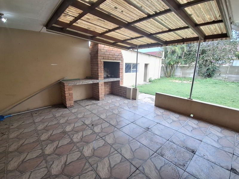 Covered outdoor patio featuring a built-in brick braai, tiled flooring, and direct access to the rear garden area.