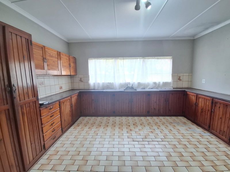 A spacious kitchen featuring traditional wooden cabinetry, tiled flooring, and a functional layout with ample counter space and a built-in pantry.