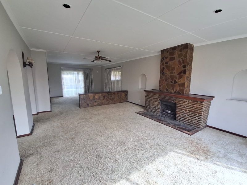 Spacious living area featuring a prominent stone fireplace, stone room divider, and neutral wall tones, offering a blank canvas for modern renovation.
