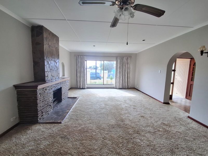 Spacious living room featuring a prominent stone fireplace, ceiling fan, and arched entryway, offering a blank canvas for modern interior updates.