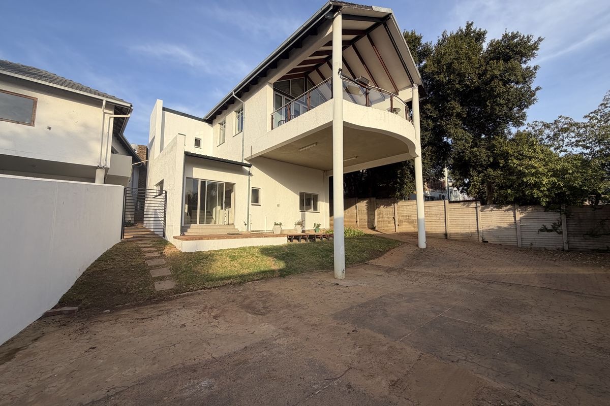 Rear view of the duet property featuring a raised balcony with glass balustrade, paved driveway area, and established boundary walls.