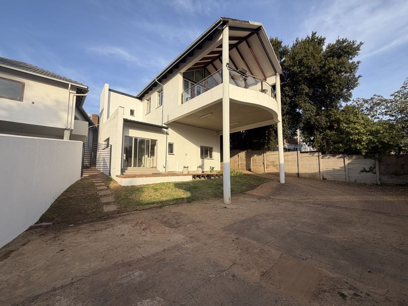 Rear view of the duet property featuring a raised balcony with glass balustrade, paved driveway area, and established boundary walls.