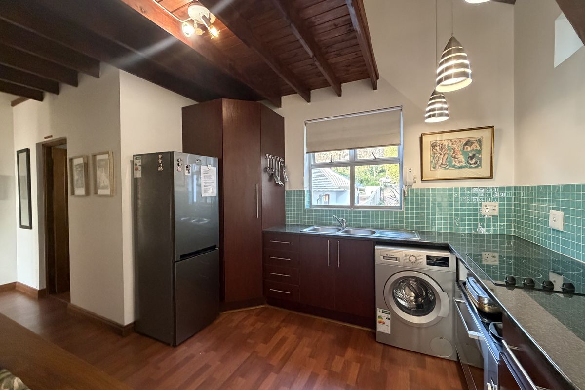A functional kitchen featuring dark wood cabinetry, laminate flooring, exposed timber ceiling beams, and a tiled splashback with integrated appliances.