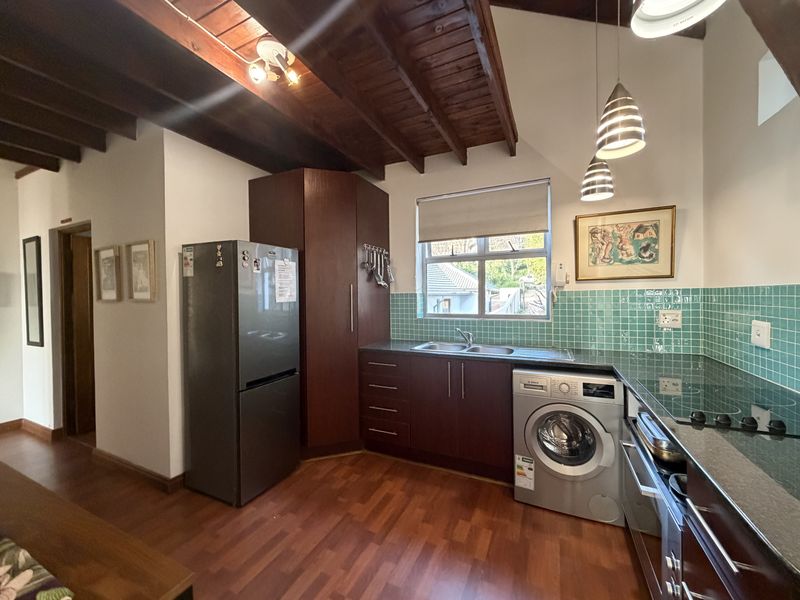 A functional kitchen featuring dark wood cabinetry, laminate flooring, exposed timber ceiling beams, and a tiled splashback with integrated appliances.