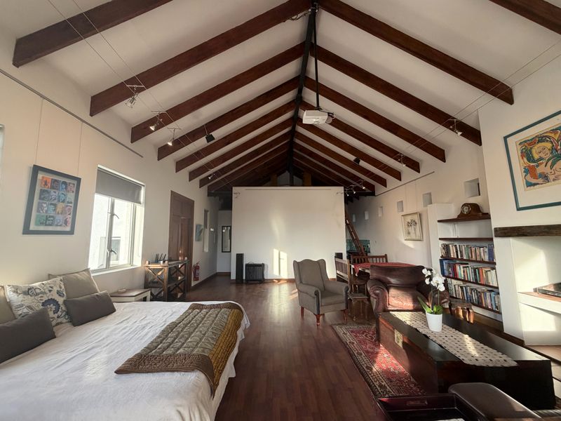 Spacious open-plan living area featuring high vaulted ceilings with exposed timber beams, hardwood flooring, and a cozy fireplace.