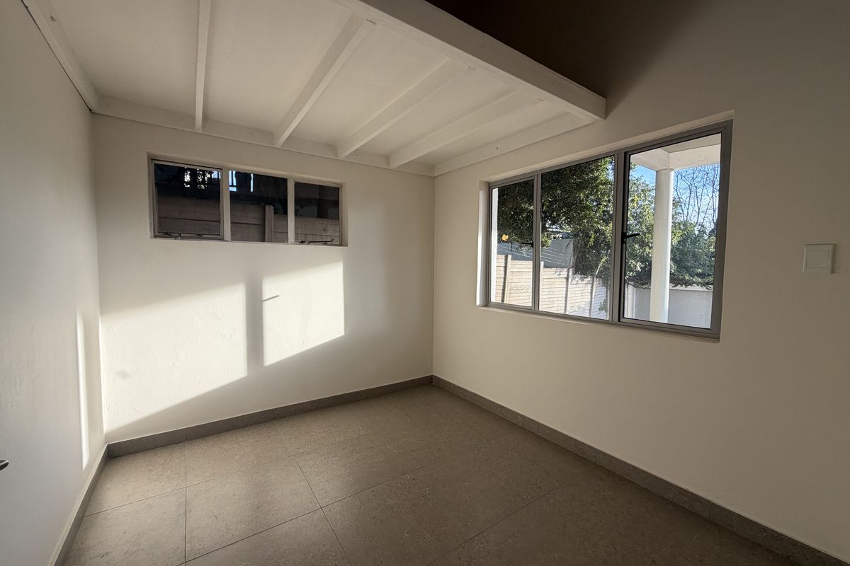 A bright, empty bedroom featuring tiled flooring, exposed beam ceiling, and large aluminium-framed windows allowing for ample natural light.