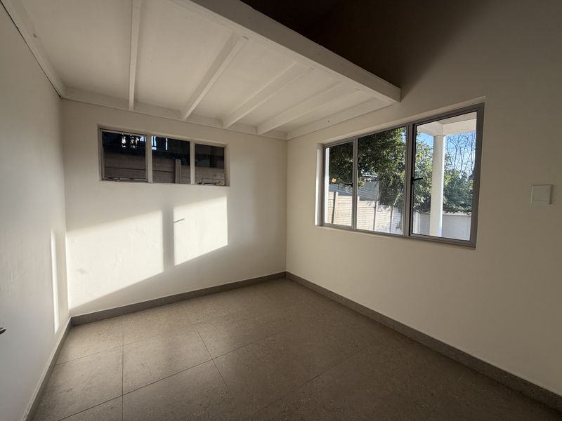A bright, empty bedroom featuring tiled flooring, exposed beam ceiling, and large aluminium-framed windows allowing for ample natural light.