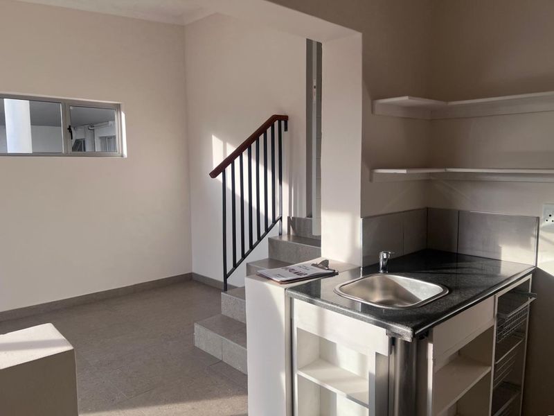 A functional scullery area featuring a stainless steel sink, granite countertop, built-in shelving, and direct access to an internal staircase.