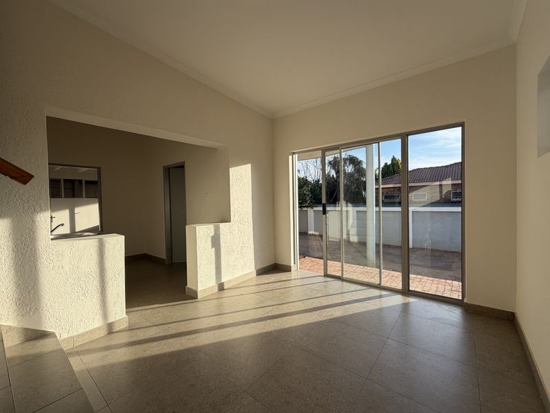Bright open-plan living area featuring neutral tiled flooring, a pass-through kitchen counter, and large sliding glass doors leading to the outdoor space.