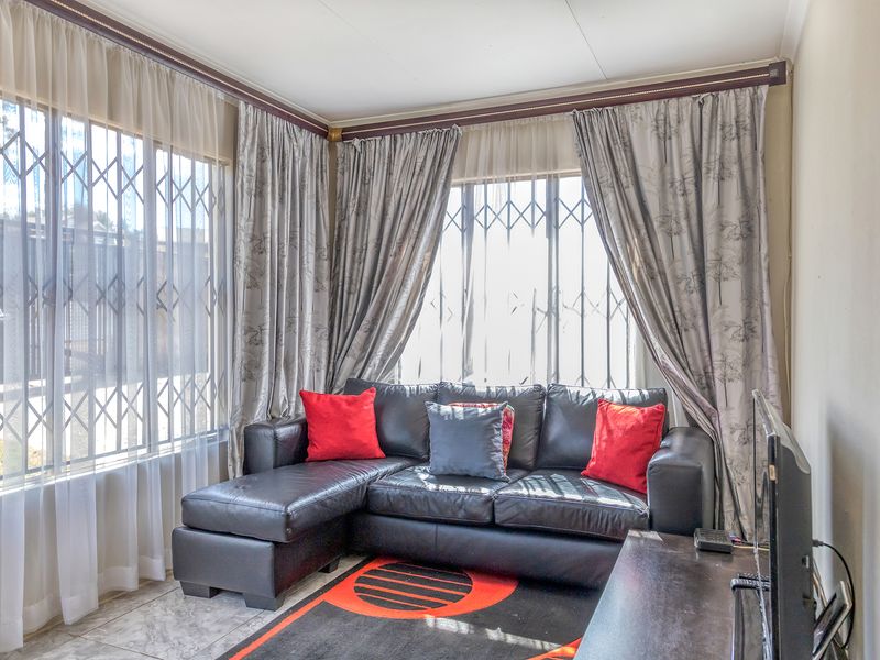 A bright living room featuring tiled flooring and large windows fitted with security gates and curtain rails.