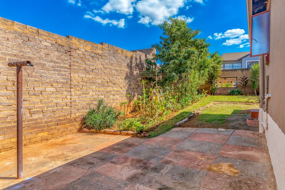A rear garden area featuring a paved patio, brick boundary wall, and lawn space, providing a functional outdoor area for the property.