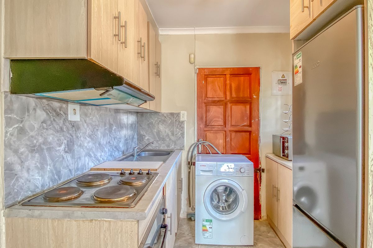 Compact kitchen featuring light wood-look cabinetry, electric hob, extractor fan, built-in oven, and integrated laundry plumbing.
