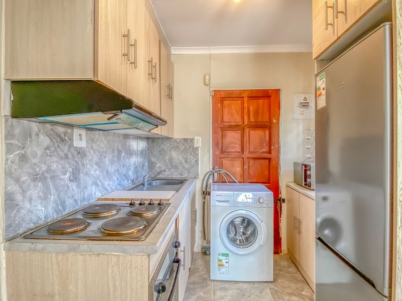 Compact kitchen featuring light wood-look cabinetry, electric hob, extractor fan, built-in oven, and integrated laundry plumbing.