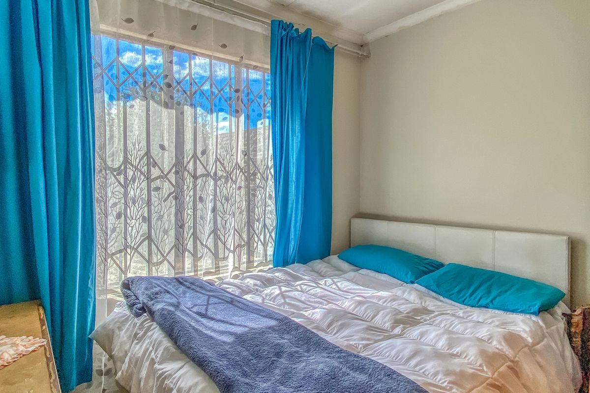 A bedroom featuring a window with a security gate and curtain rails, showing signs of wear on the ceiling.