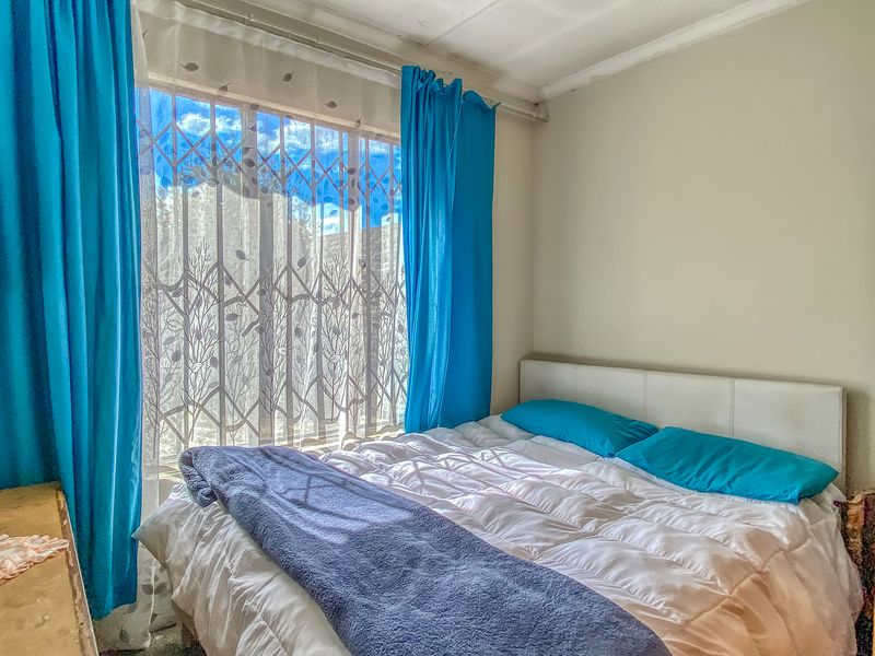 A bedroom featuring a window with a security gate and curtain rails, showing signs of wear on the ceiling.