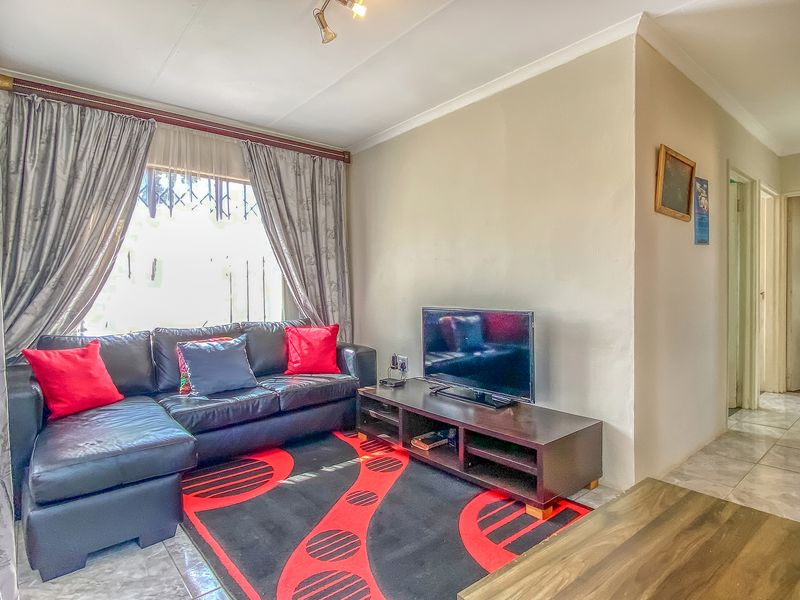 A living room featuring tiled flooring, cove cornicing, and security bars on the window, providing a functional and lived-in space.