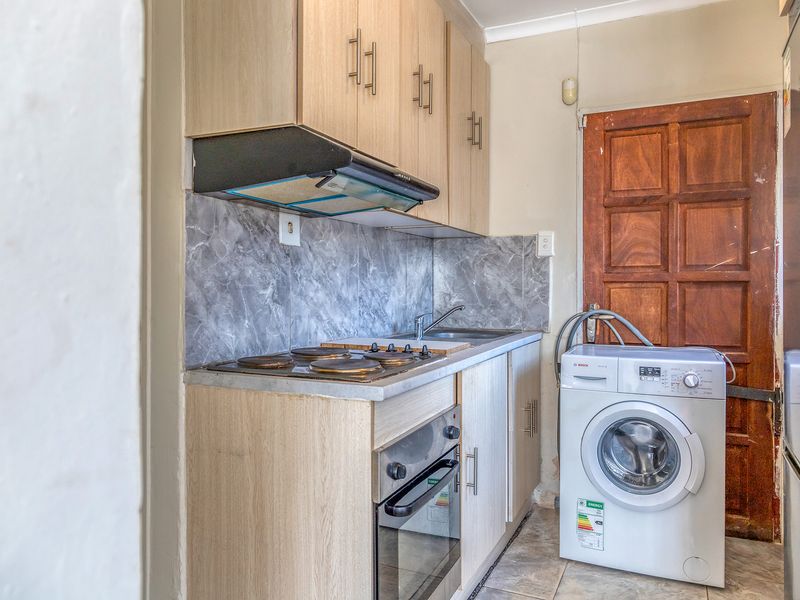 Compact scullery featuring built-in cabinetry, electric hob, oven, extractor fan, and dedicated space for laundry appliances with marble-effect splashback.