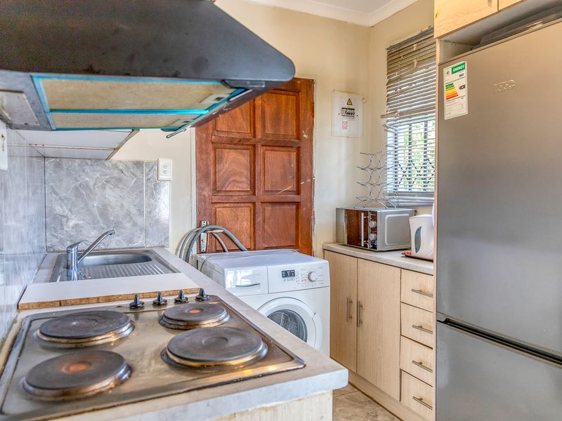 Compact kitchen featuring an electric hob, extractor fan, stainless steel sink, and light wood-finish cabinetry with integrated laundry appliance space.