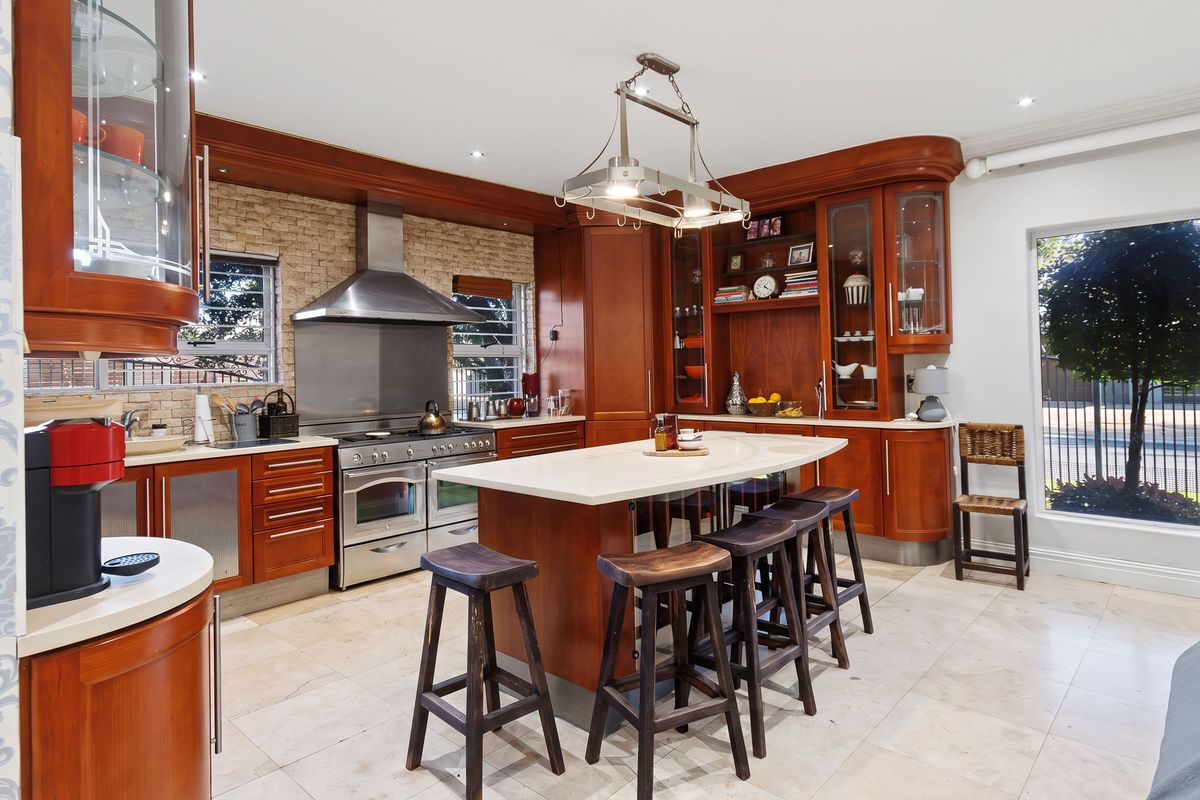 Spacious kitchen featuring warm wood cabinetry, a central island with stone countertops, stainless steel range cooker, and stone tile flooring.