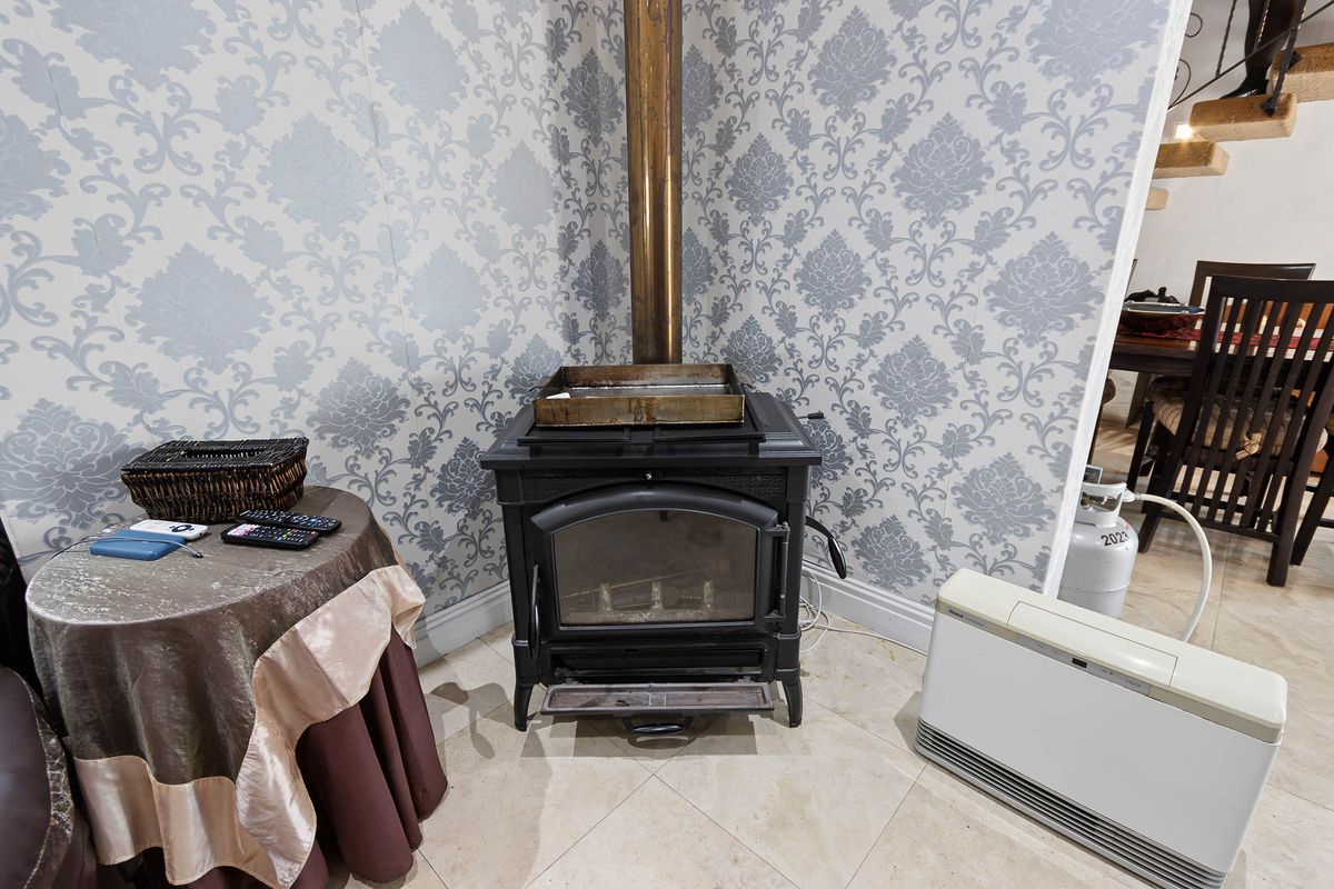 A living area featuring a cast iron wood burning stove with a flue pipe, set against patterned wallpaper and tiled flooring.