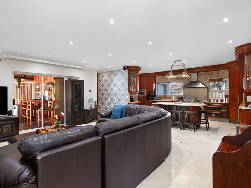 Spacious open-plan living and kitchen area featuring stone tile flooring, recessed lighting, and a well-appointed kitchen with a central island and brick feature wall.