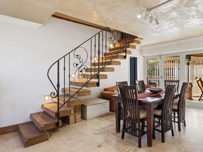 Dining area featuring stone tile flooring, a wrought iron staircase with carpeted treads, and sliding glass doors leading to an outdoor space.
