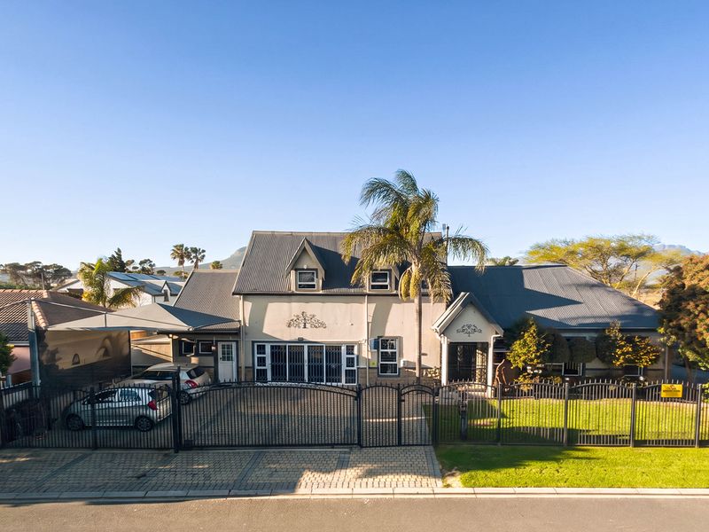 Aerial view of a residential property featuring a corrugated metal roof, dormer windows, a paved driveway with a carport, and secure perimeter fencing.