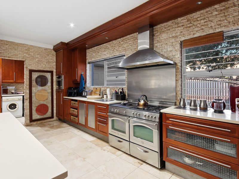 Spacious kitchen featuring warm wood cabinetry, stone tile flooring, a large stainless steel gas range with extractor, and integrated laundry facilities.