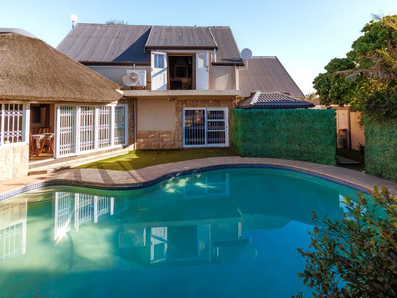 Rear exterior view featuring a swimming pool, stone-clad facade, and a combination of metal and thatch roofing with an upper-level balcony.
