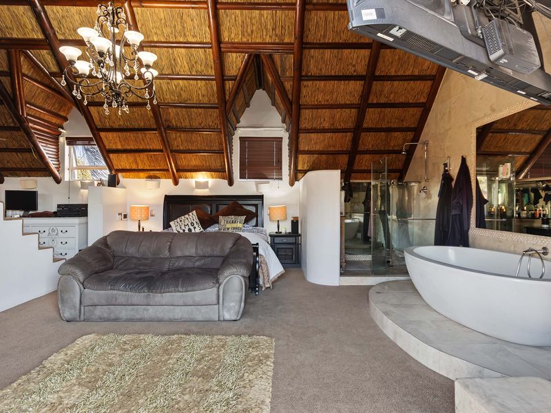 Spacious bedroom featuring a unique exposed thatch ceiling with timber rafters, an integrated en-suite bathroom with a freestanding tub and glass shower.
