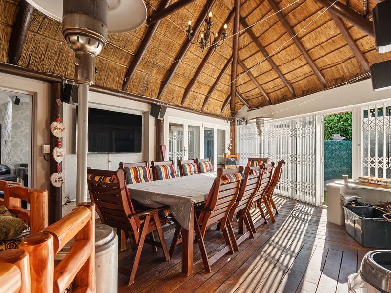 A spacious covered patio featuring a high thatched roof with exposed timber rafters and durable timber decking, ideal for outdoor entertaining.
