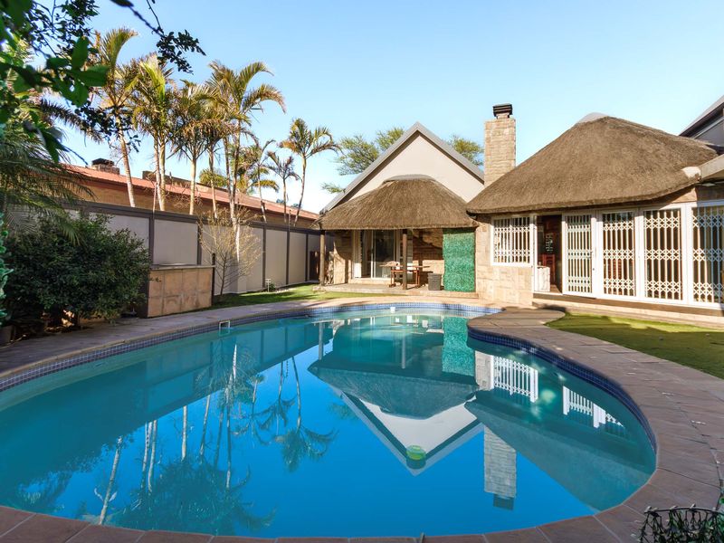 A well-maintained outdoor pool area featuring a swimming pool, stone chimney, and traditional thatch roof architecture with secure access points.