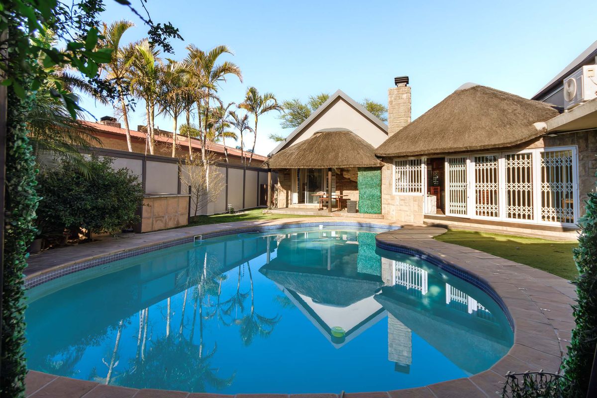 A well-maintained outdoor pool area featuring a swimming pool, stone chimney, and traditional thatch roof architecture with secure access points.