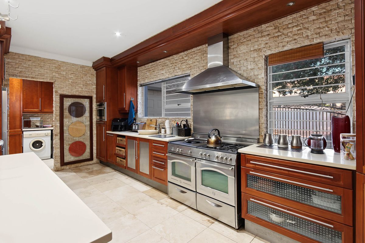 Spacious kitchen featuring warm wood cabinetry, stone tile flooring, a large stainless steel gas range with extractor, and integrated laundry facilities.