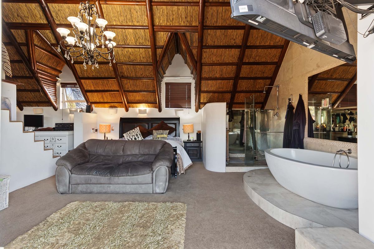 Spacious bedroom featuring a unique exposed thatch ceiling with timber rafters, an integrated en-suite bathroom with a freestanding tub and glass shower.