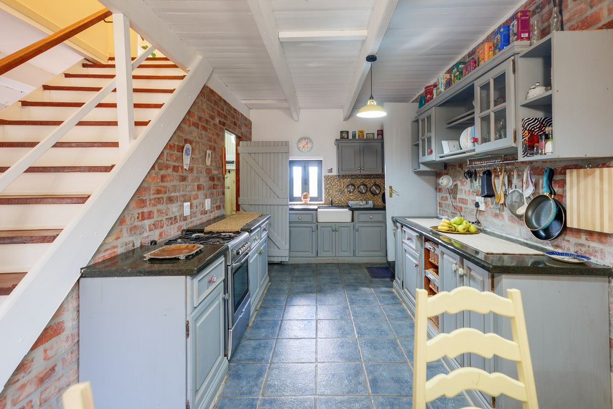 Charming rustic kitchen featuring exposed brick walls, farmhouse sink, gas stove, and built-in cabinetry, complemented by a timber staircase and exposed beam ceiling.