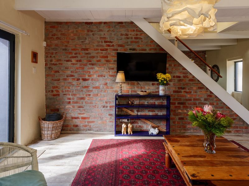 A cozy living room featuring an exposed brick feature wall, timber flooring, and a staircase, with direct access to the outdoor area via sliding doors.