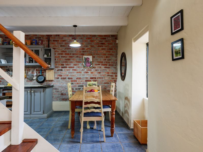 Open plan kitchen and dining area featuring exposed brick walls, timber staircase, tiled flooring, and exposed beam ceilings with characterful finishes.