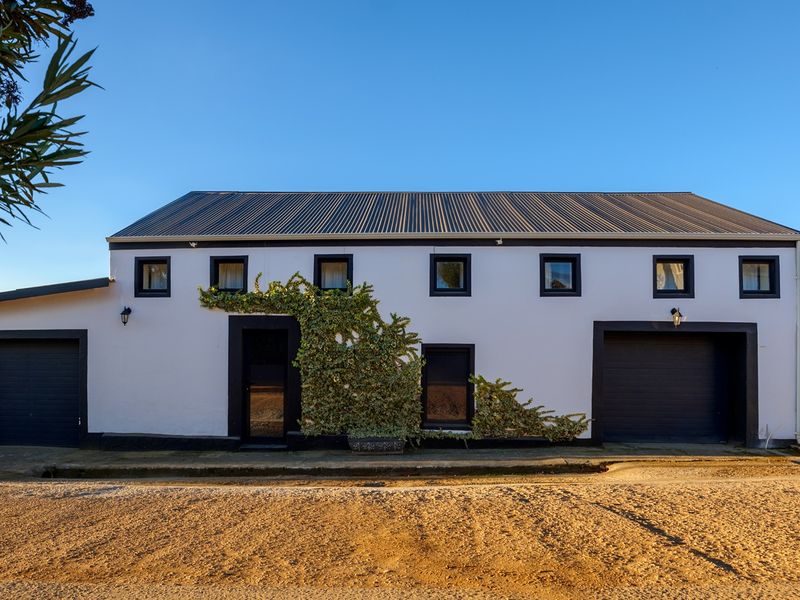 Front elevation of a modern house featuring a corrugated metal roof, two garage doors, and clean white facade with dark trim.