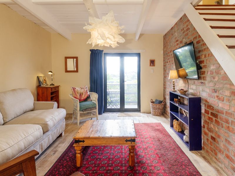 Cozy living room featuring an exposed brick feature wall, timber ceiling beams, and direct access to an outdoor area through glass french doors.