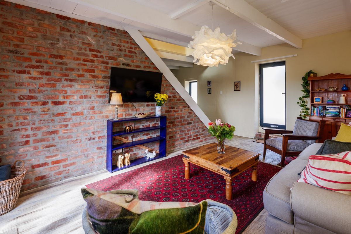 A cozy living room featuring an exposed brick feature wall, timber ceiling beams, and light wood flooring, creating a warm and rustic atmosphere.