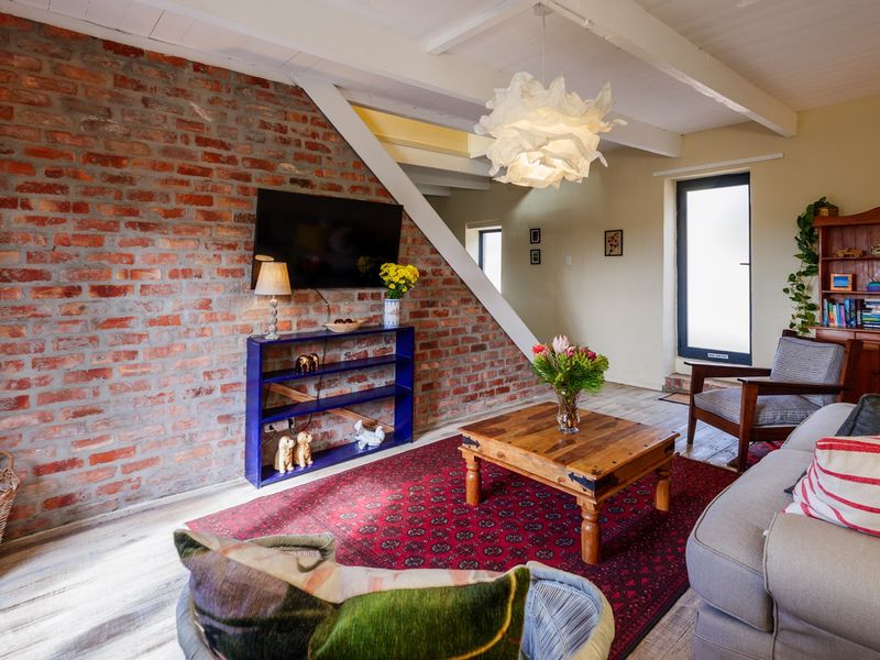A cozy living room featuring an exposed brick feature wall, timber ceiling beams, and light wood flooring, creating a warm and rustic atmosphere.