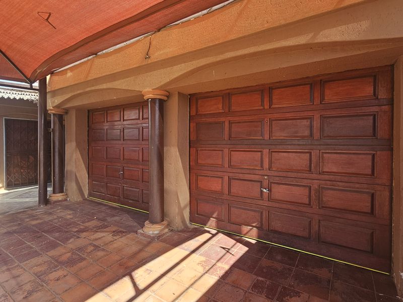 A double garage featuring wooden panel doors, tiled flooring, and structural columns, protected by an overhead shade sail.