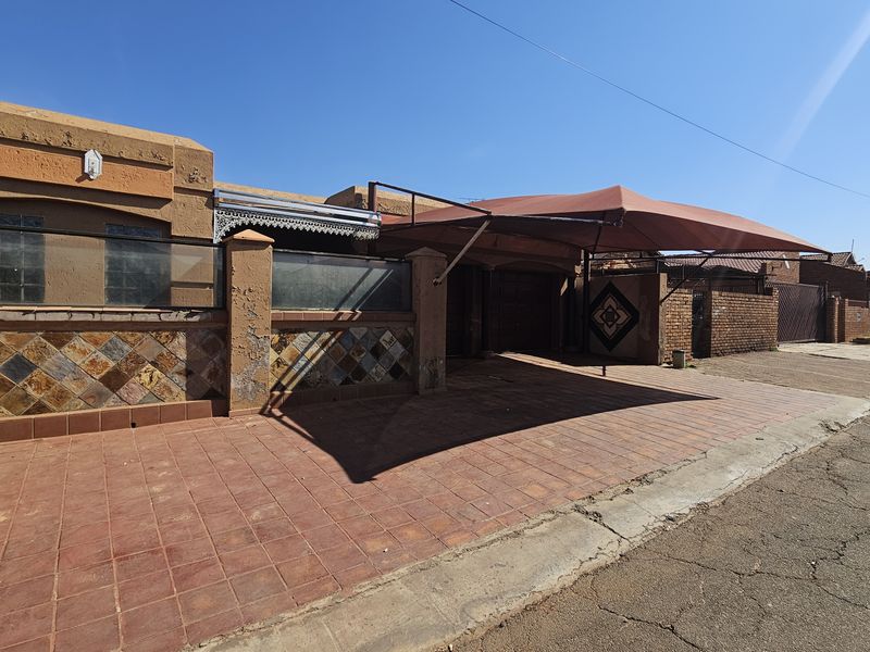 Front exterior view of the property featuring a paved driveway, shade sail carport, and boundary wall with decorative slate tile accents.
