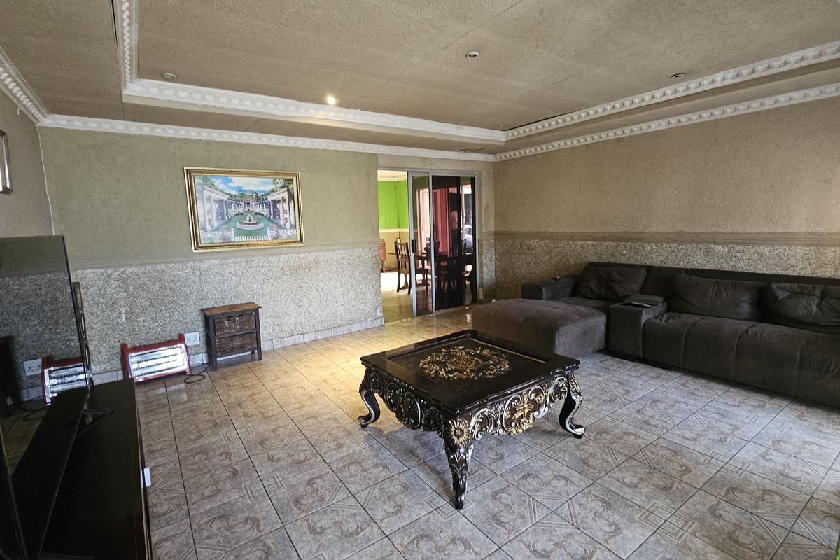 Spacious living room featuring tiled flooring, decorative ceiling cornices, and a sliding glass door leading to an adjacent room.