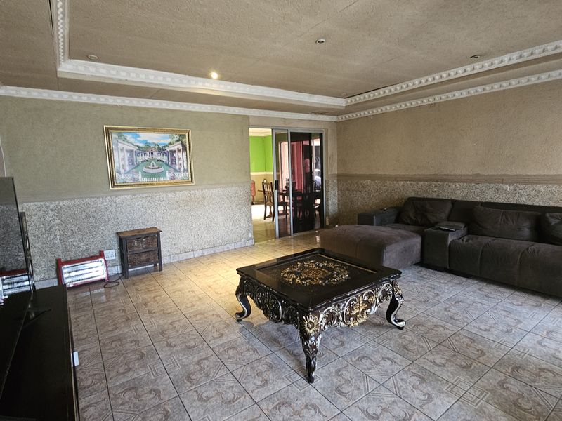 Spacious living room featuring tiled flooring, decorative ceiling cornices, and a sliding glass door leading to an adjacent room.