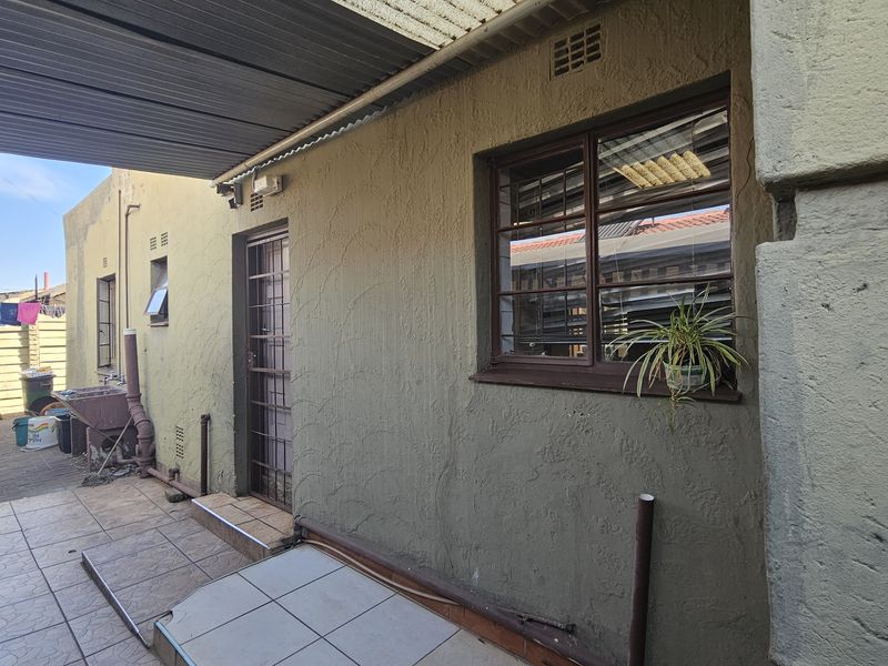 Rear exterior view of the property featuring a covered patio area, security gates, and burglar bars on the windows.